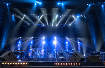 eine blaubeleuchtete Konzertbühne mit Traversen, Instrumenten und Lautsprechern.